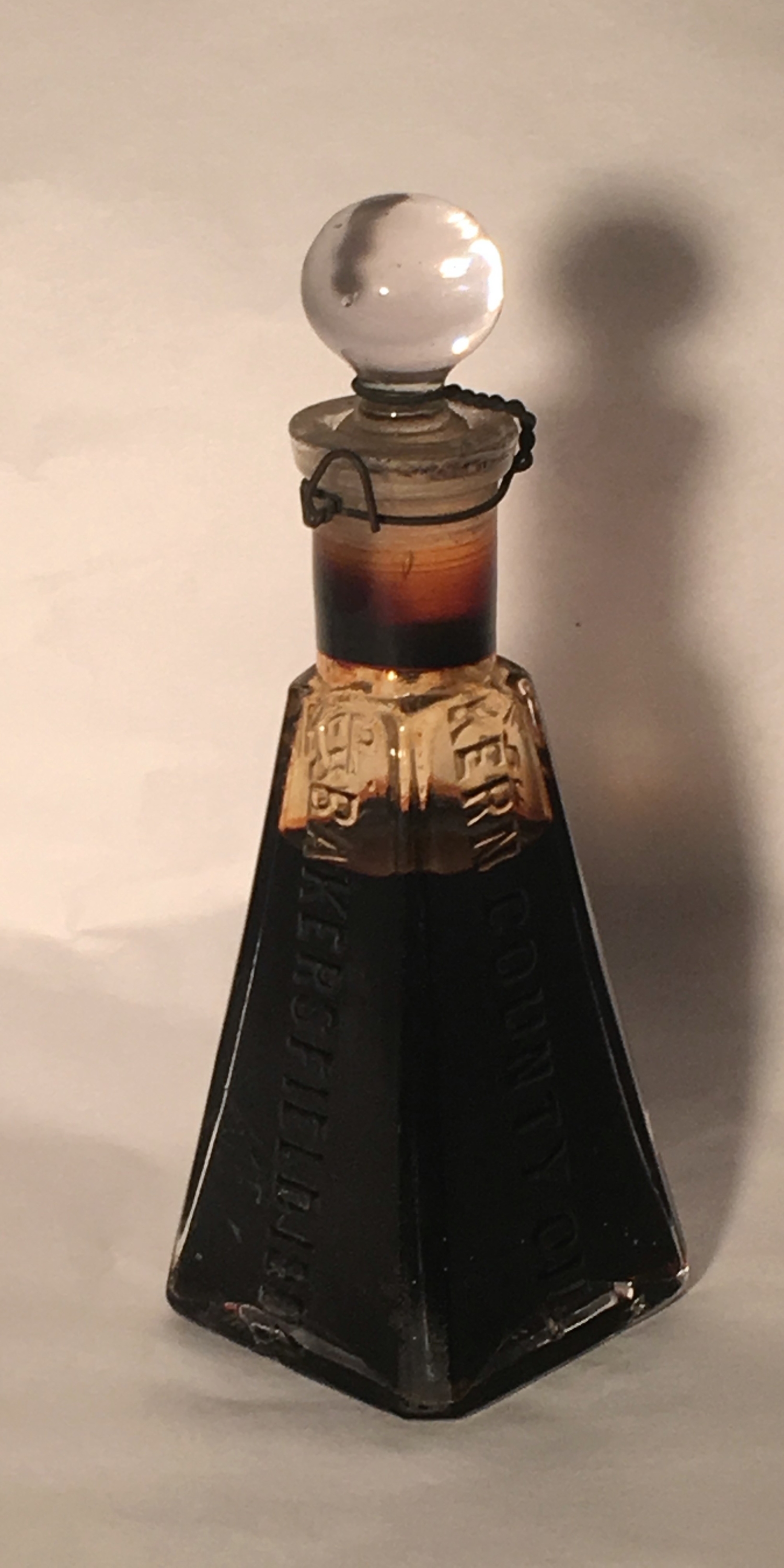 A four sided glass jar with a stopper filled with black oil.