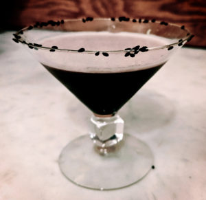 A black liquid in a martini glass lined with a black sesame seed rim.