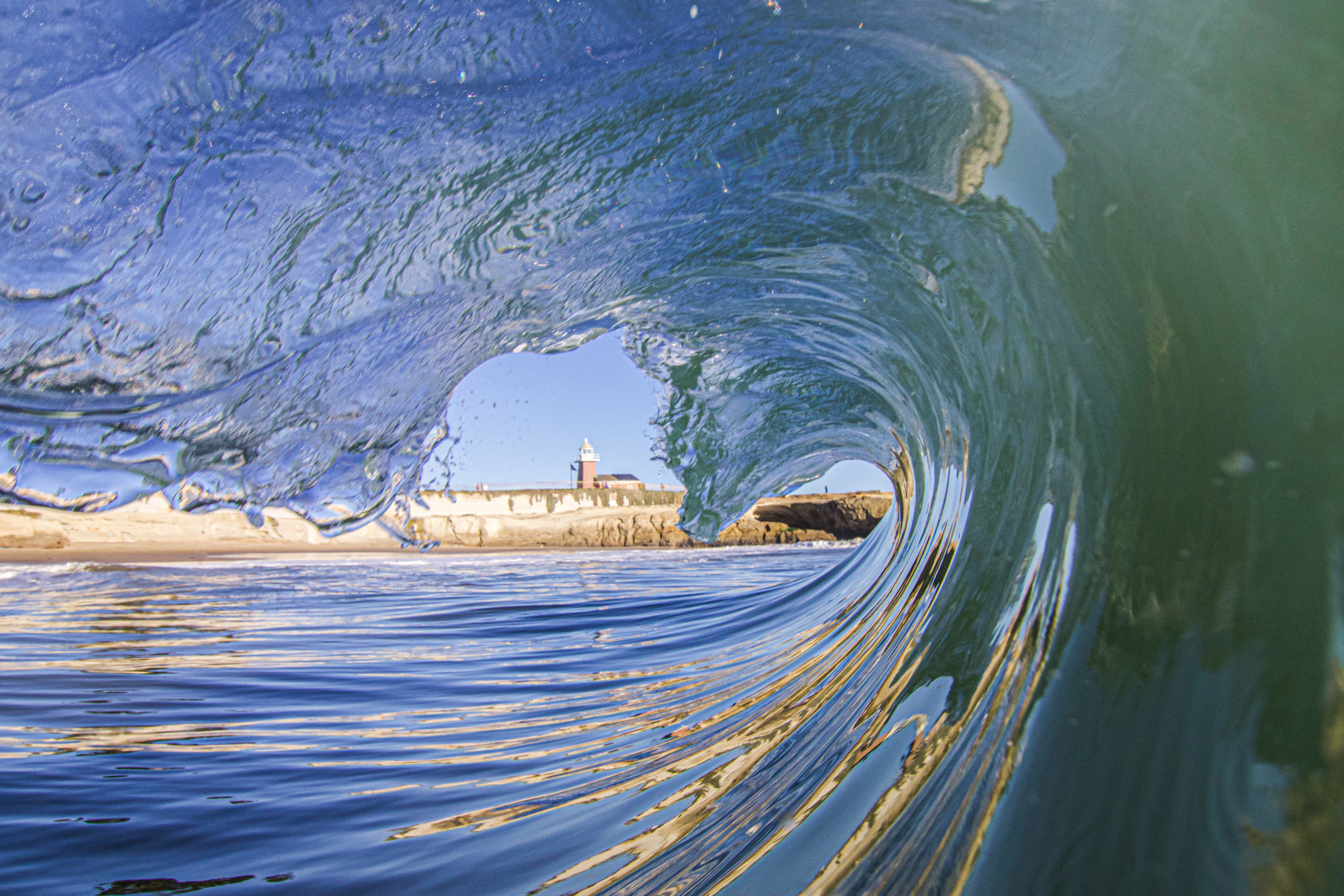 A lighthouse is framed by a cresting wave.