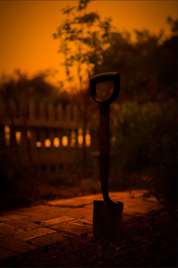 A shovel shoved into the dirt stands tall in a dark orange glow.