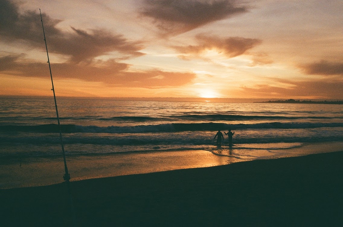 A faded image of a golden sky over the ocean, with two people silhouetted on the shore.