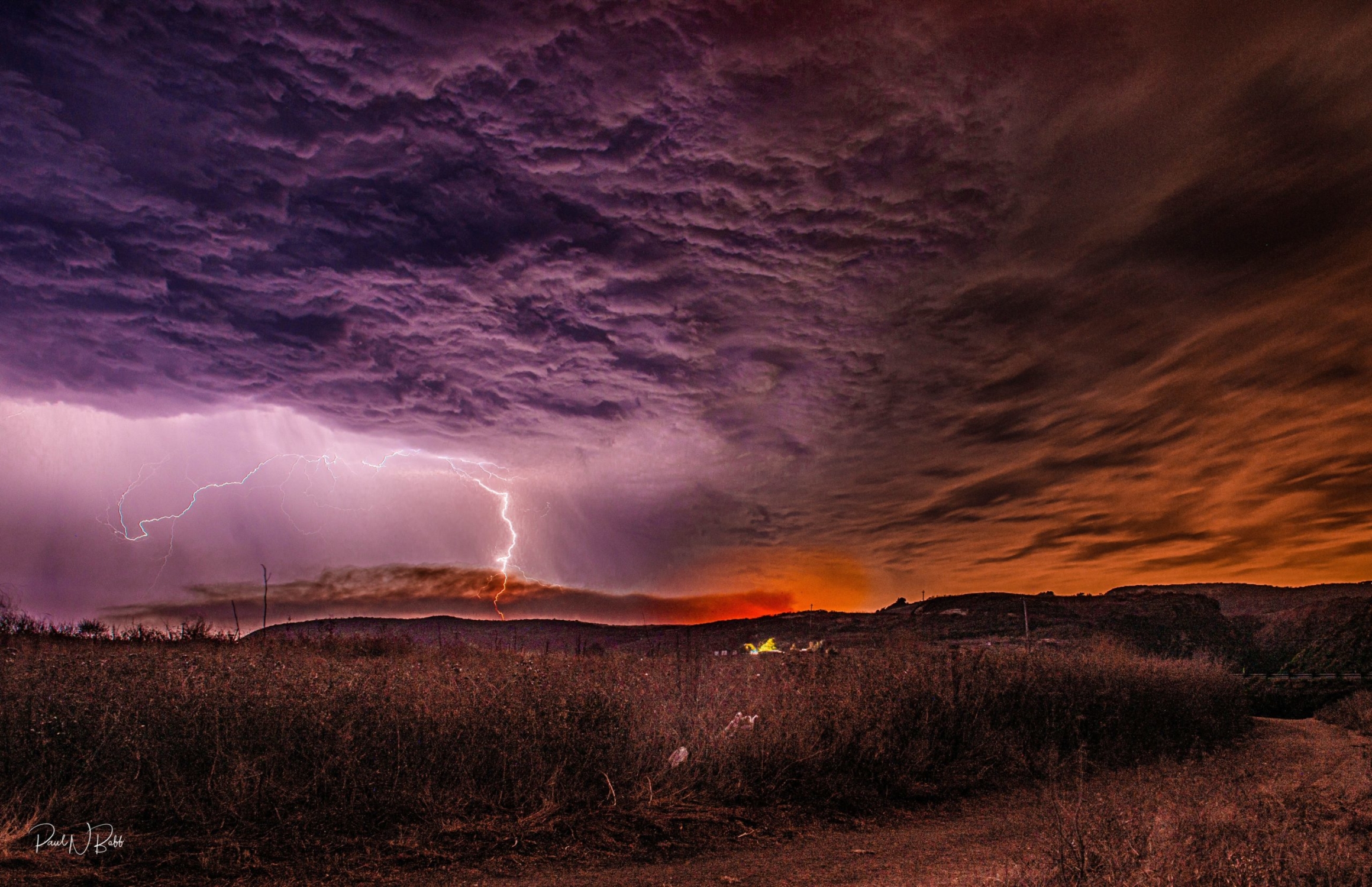 To the left is lightning traveling down from a purple cloud, while to the right is the red glow of fire.