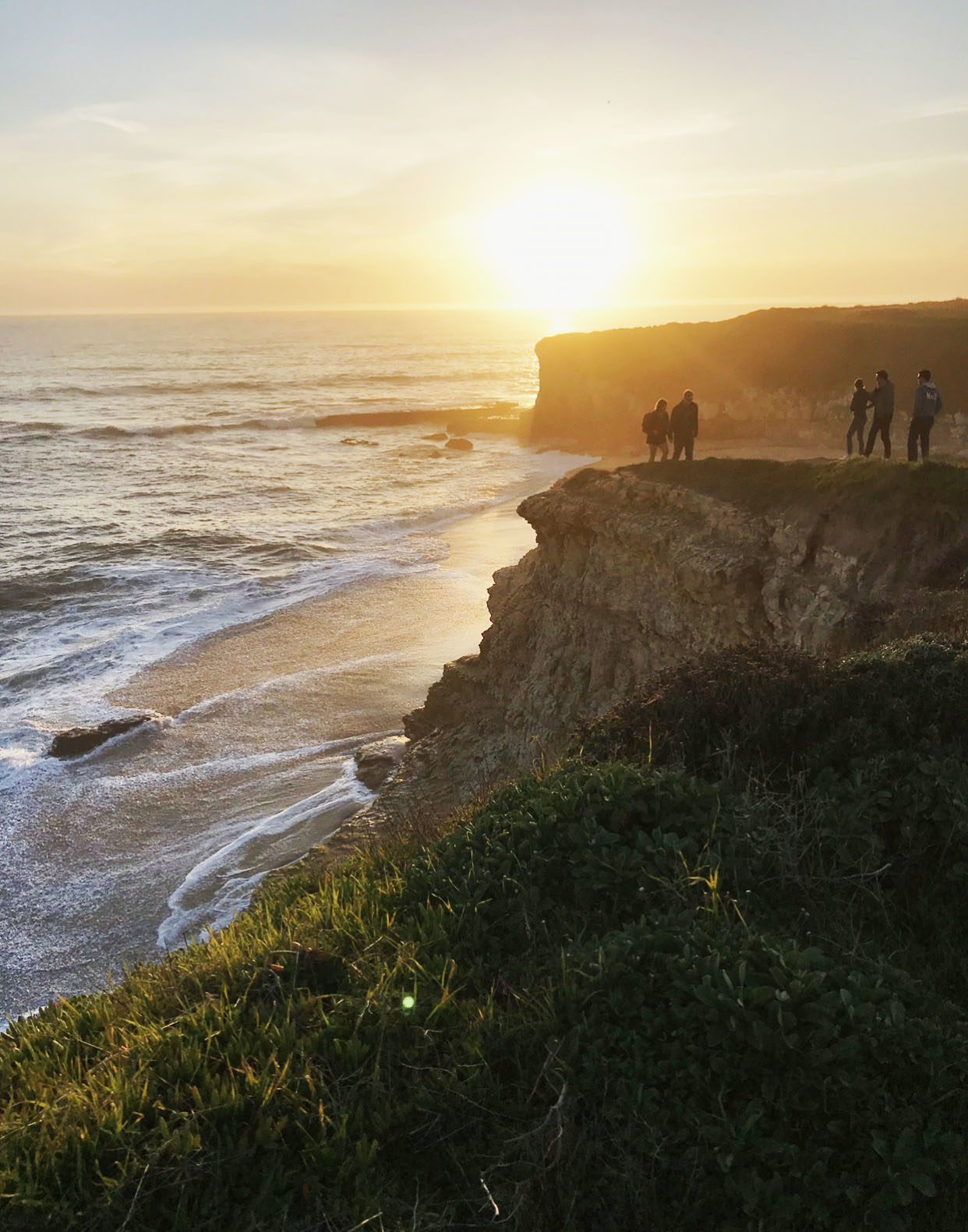 A series of tall cliffs speckled with people along the coast with the sunsetting in the distance