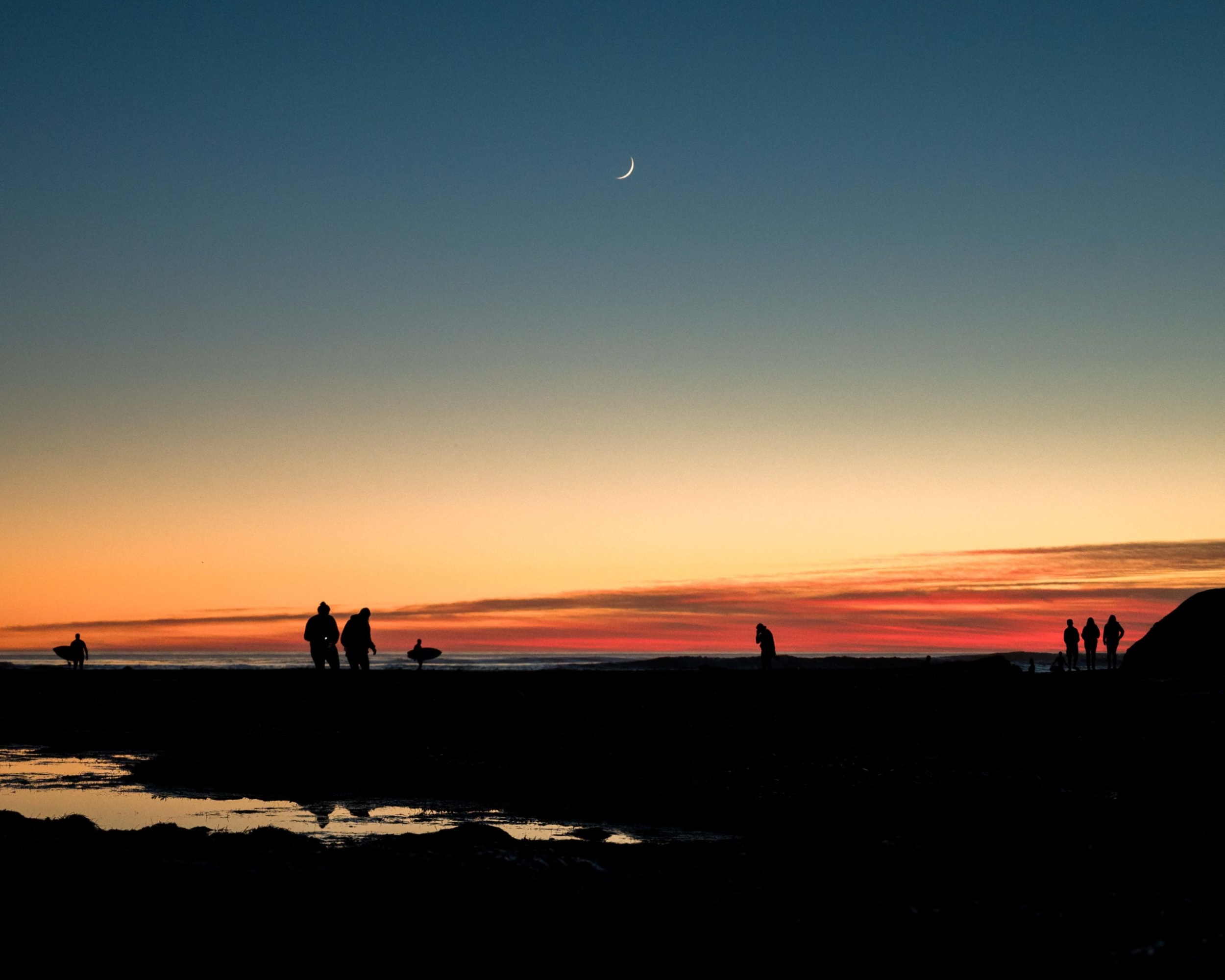 Silhouettes of people in the distance exploring the intertidal zone at sunset.