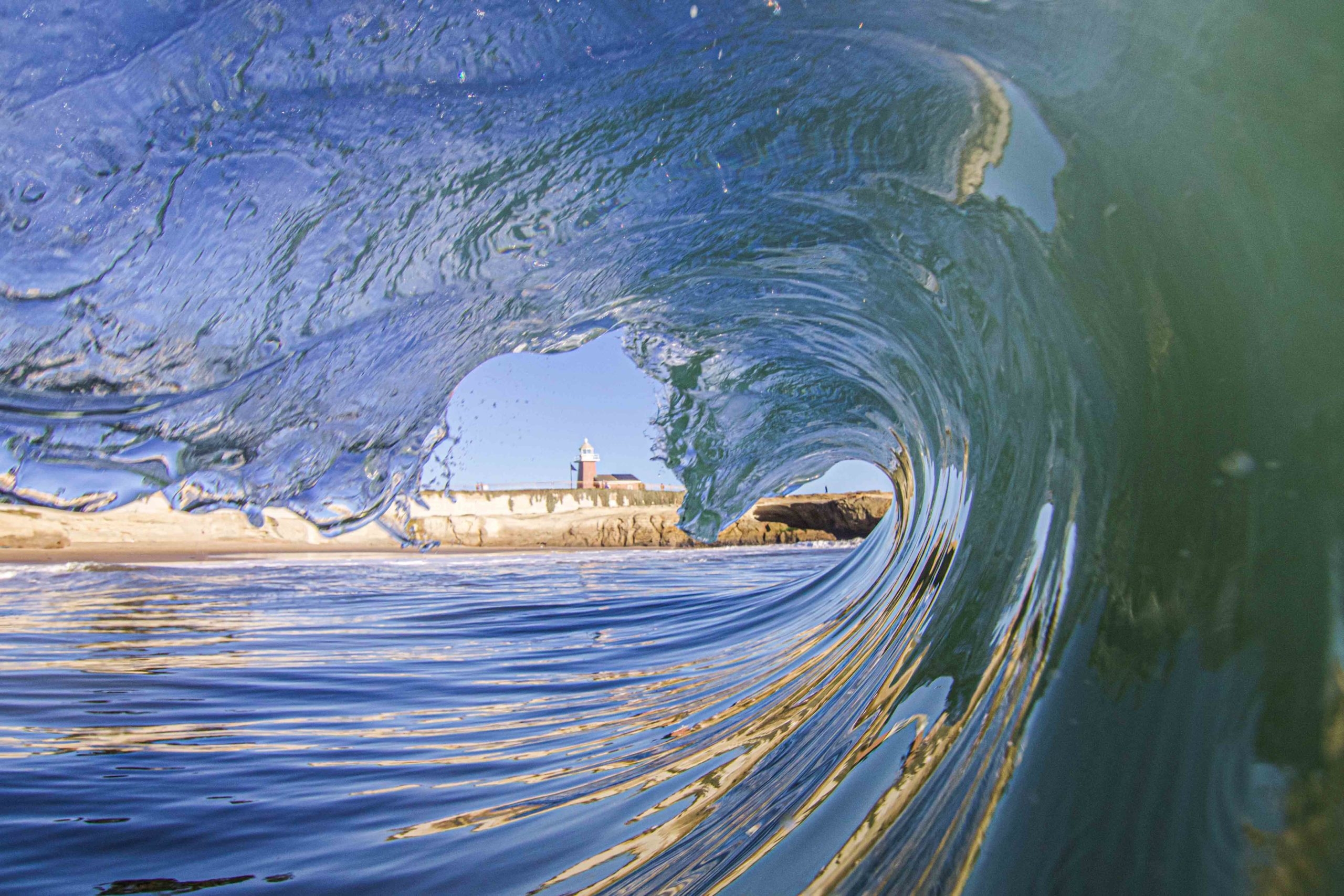 A lighthouse is framed by a cresting wave.