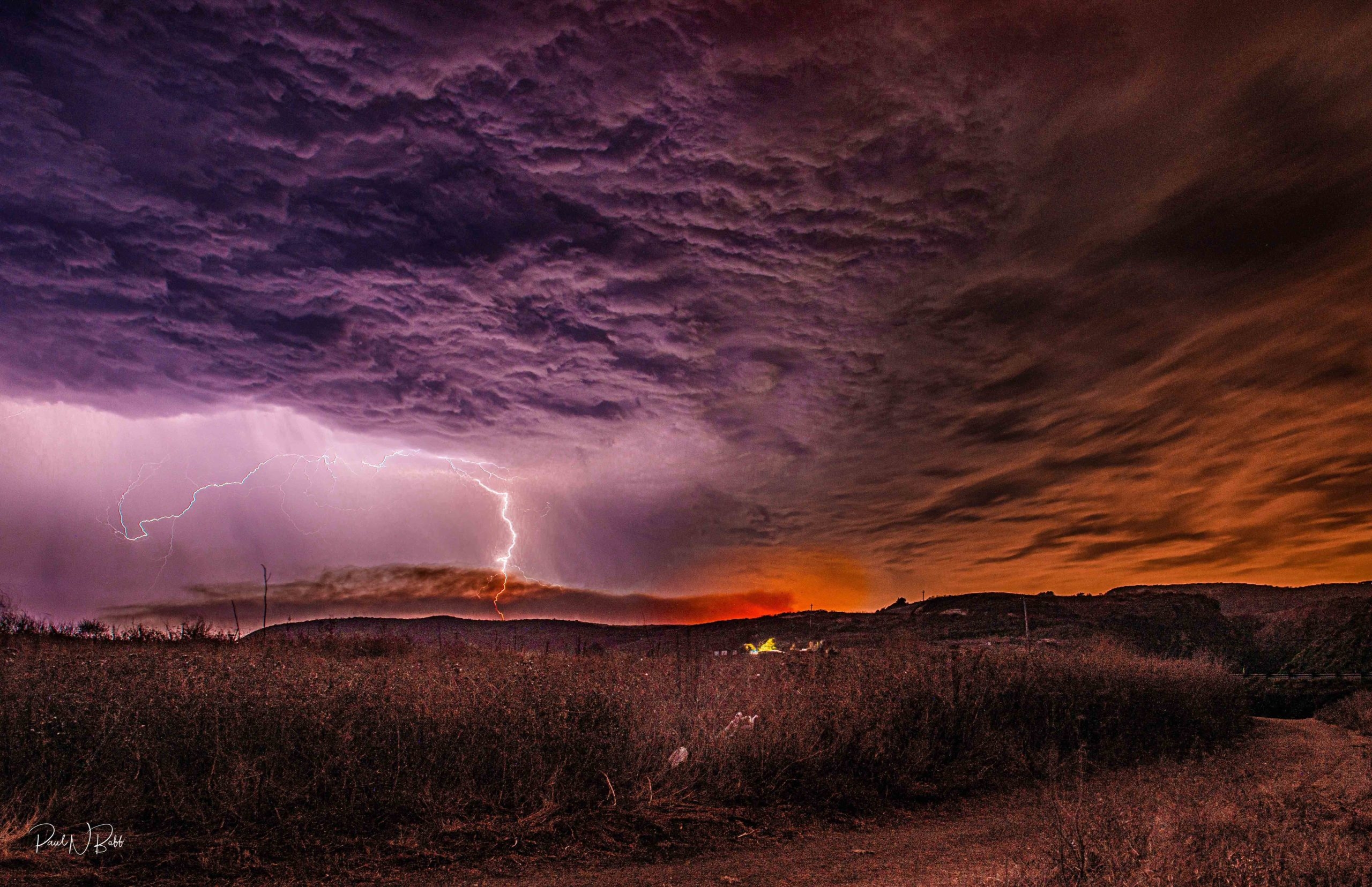 To the left is lightning traveling down from a purple cloud, while to the right is the red glow of fire.