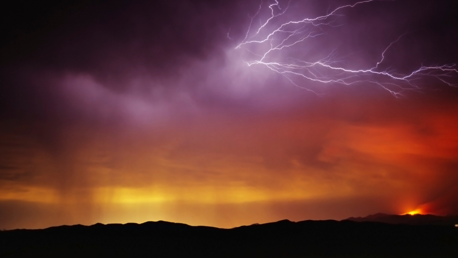 Lightning flashes through purple clouds over the horizon glowing orange.